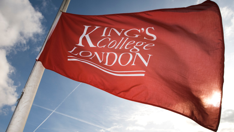 The King's College London logo adorns a red flag, flying in bright sunshine.