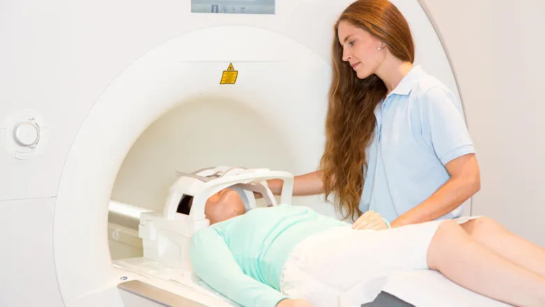Female patient lying in an MRI brain scanning machine with female doctor assisting