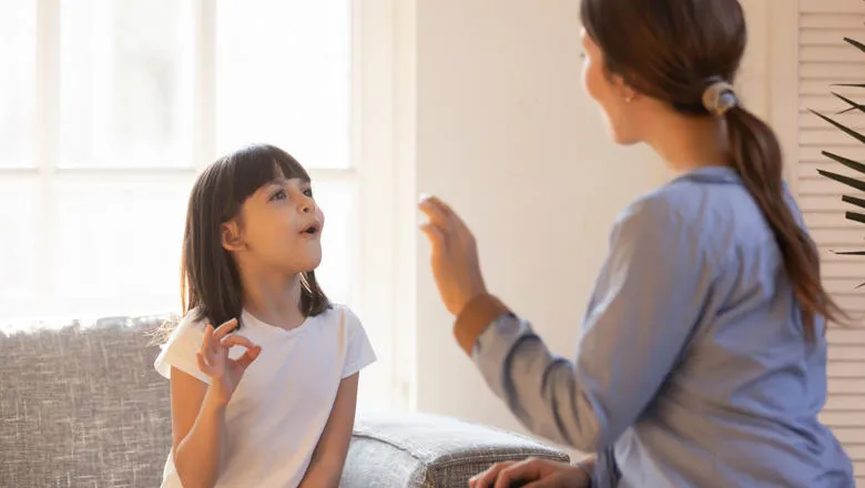 Woman making an 'ok' hand gesture at a small girl who is copying her