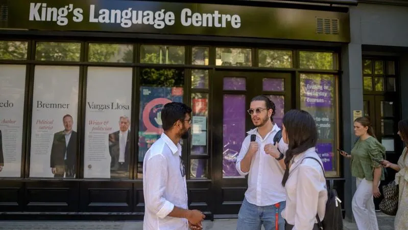 Three students stand outside the King's Language Centre, engaged in conversation under a clear blue sky.