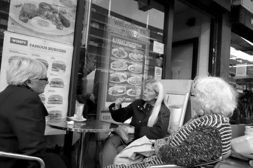 Three women sitting down outside in a cafe in watney market - black and white