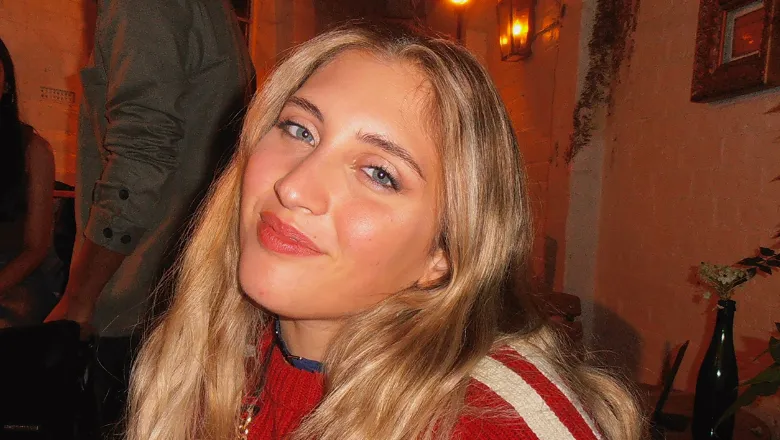 Michelle illuminated by the camera flash, wearing a red top with two white strips on the shoulder and smiling at the camera