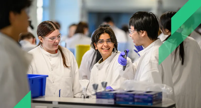 Three undergraduate students smile as they work in a lab