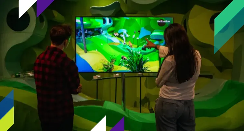 Two visitors interact with a screen showing a video game