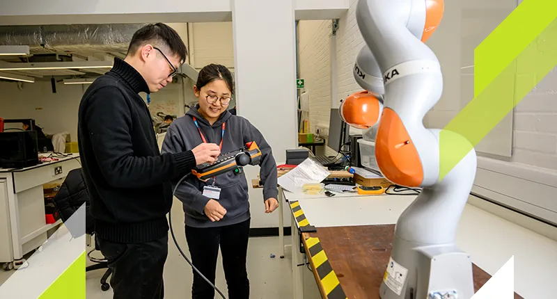 Two post graduate students look at the controls for a large robotic arm