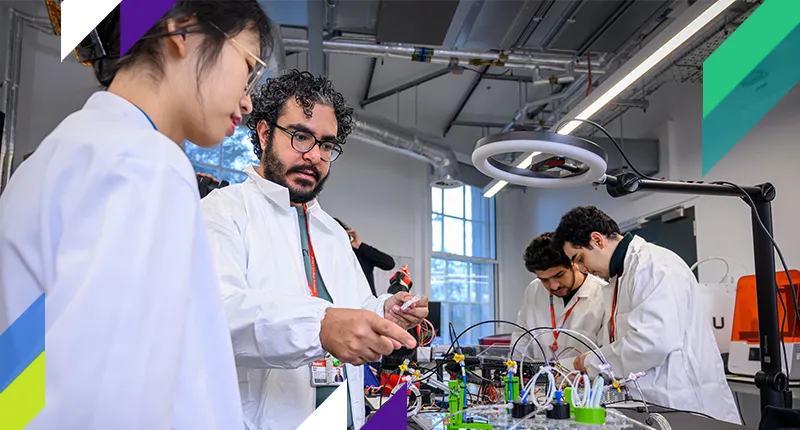 Four students in lab coats work on an engineering project