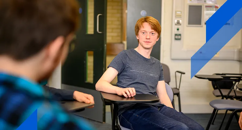 A PhD student sitting at a desk participates in a discussion