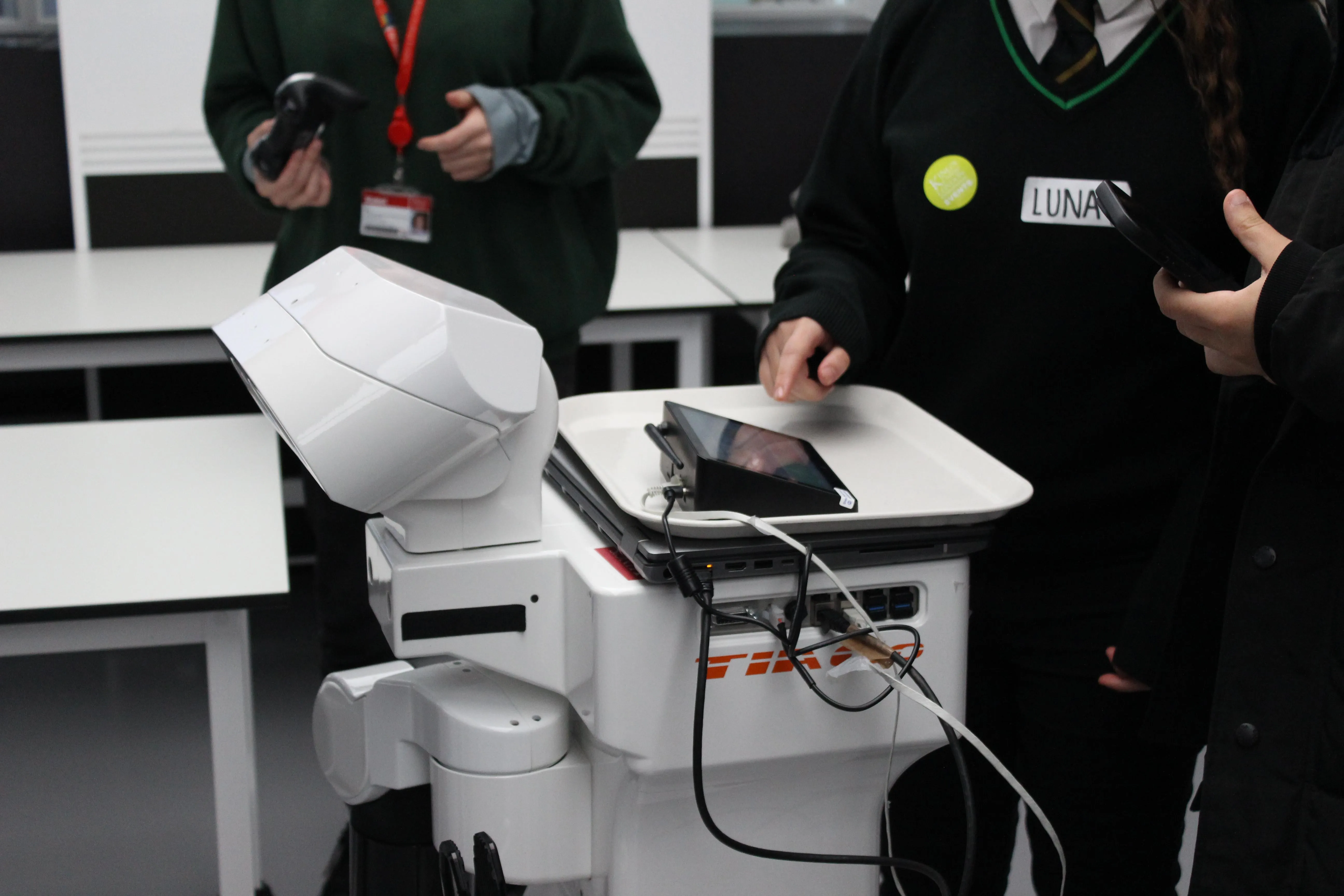 A child touches a screen that sits on top of a white robot called Tiago.