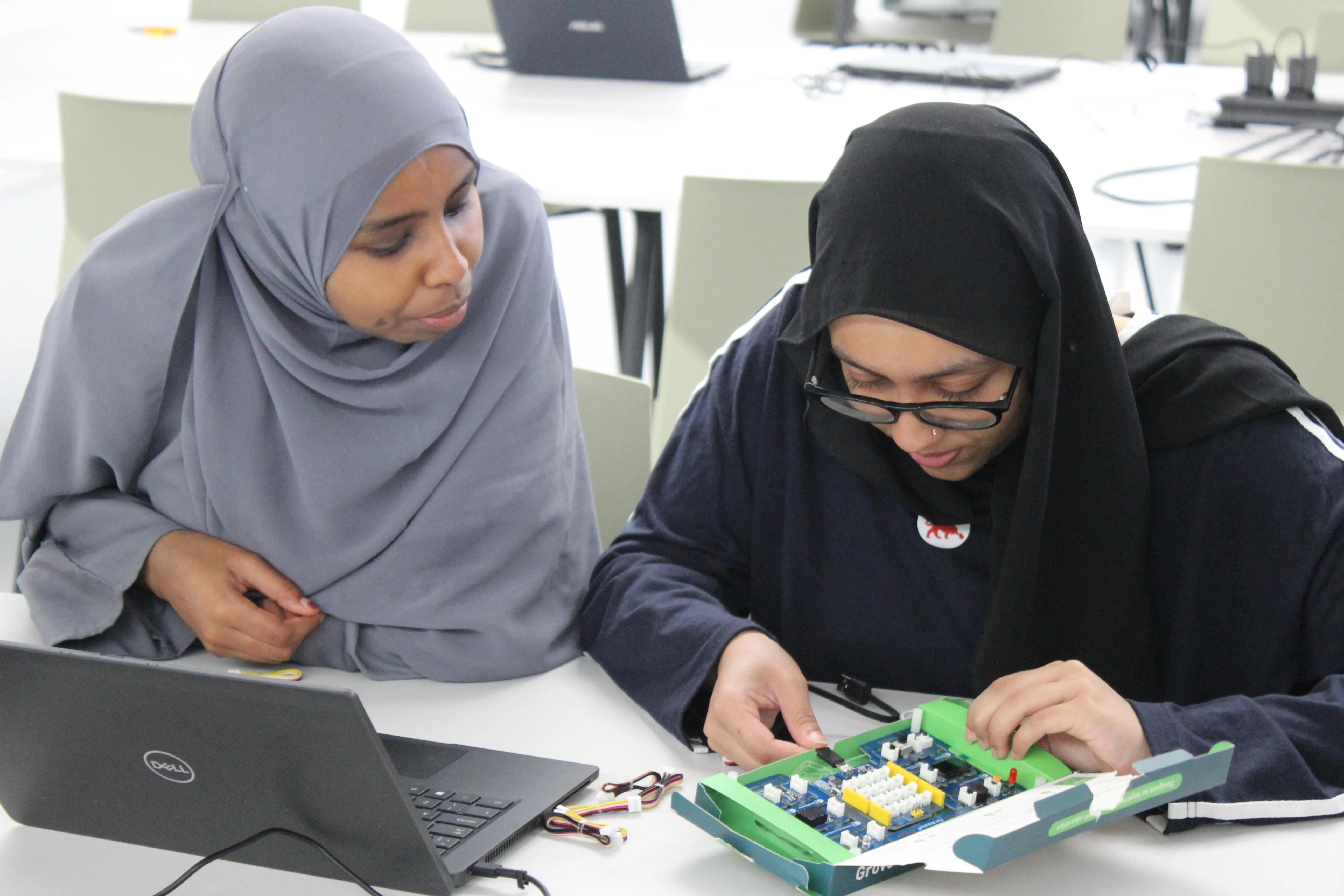 Two girls are working on an microcontroller connected to a computer