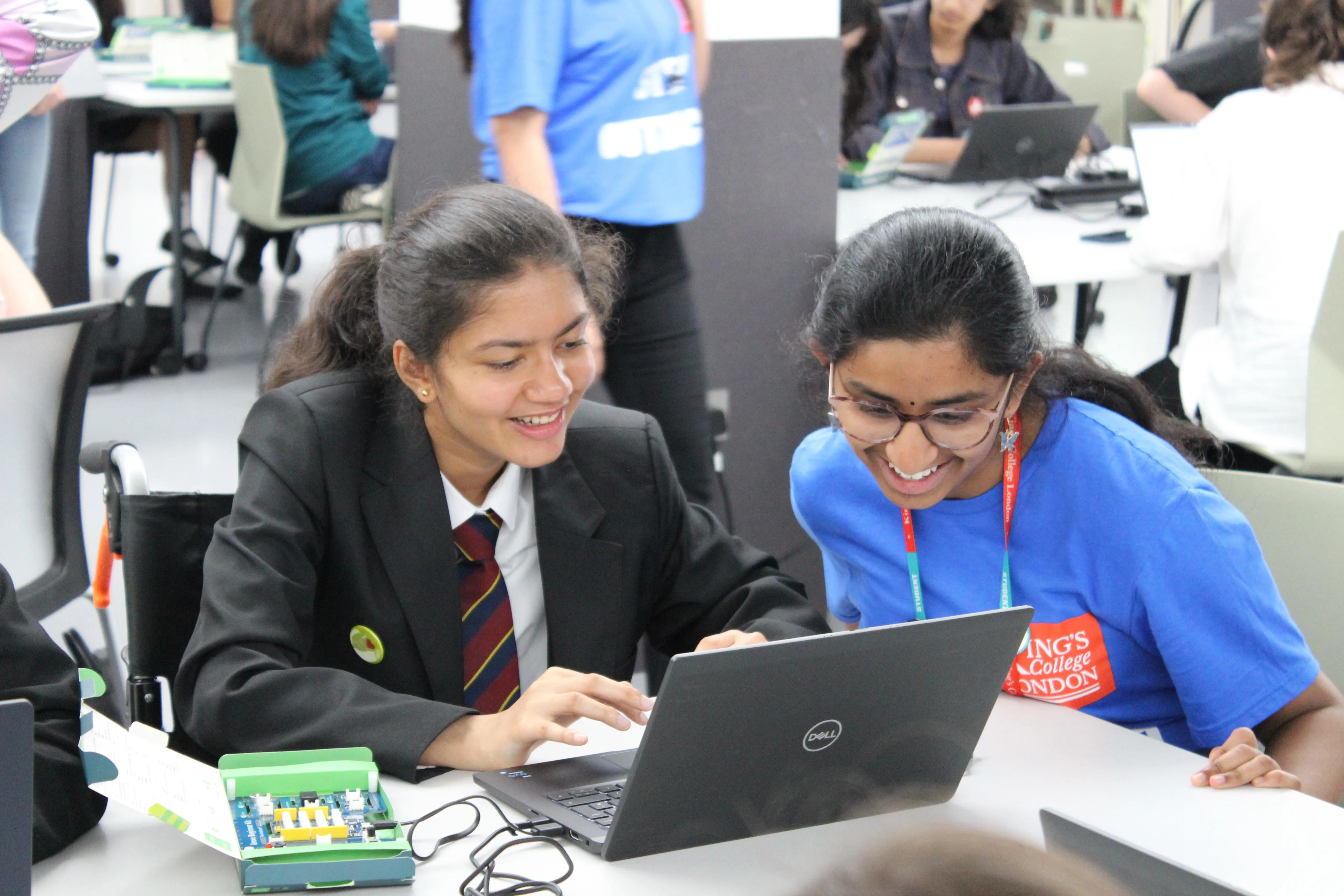 A female student ambassador is explaining something on a computer to a girl on a wheelchair