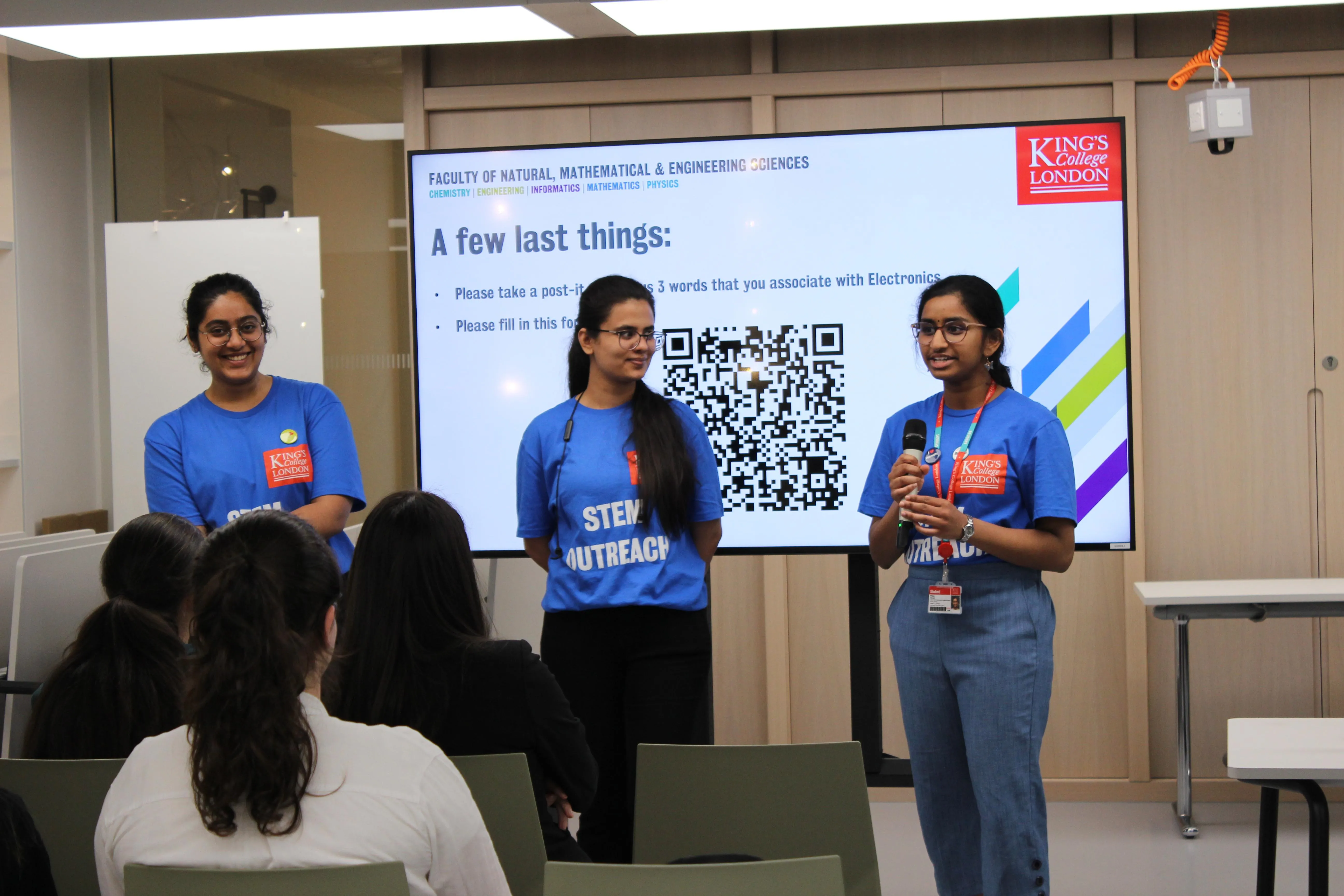 Three female student ambassadors are talking in front of a group of school girls