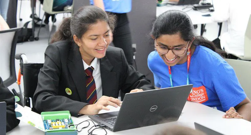 A young woman is explaining something on a computer to a girl who is using a wheelchair