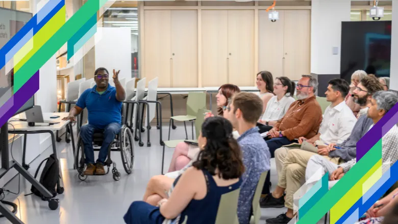 A lecturer sits and presents to a room to people sitting in rows.