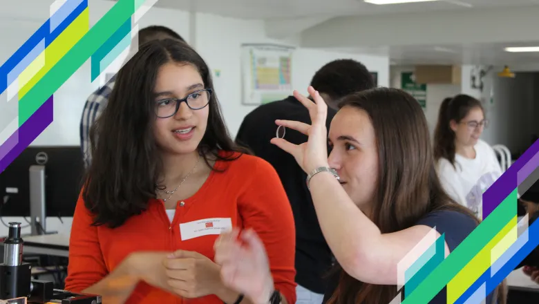 A girl looks through a lens while another girl watches