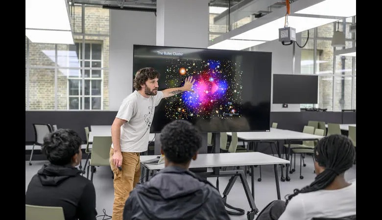A presenter points an in image of a starry galaxy on a screen