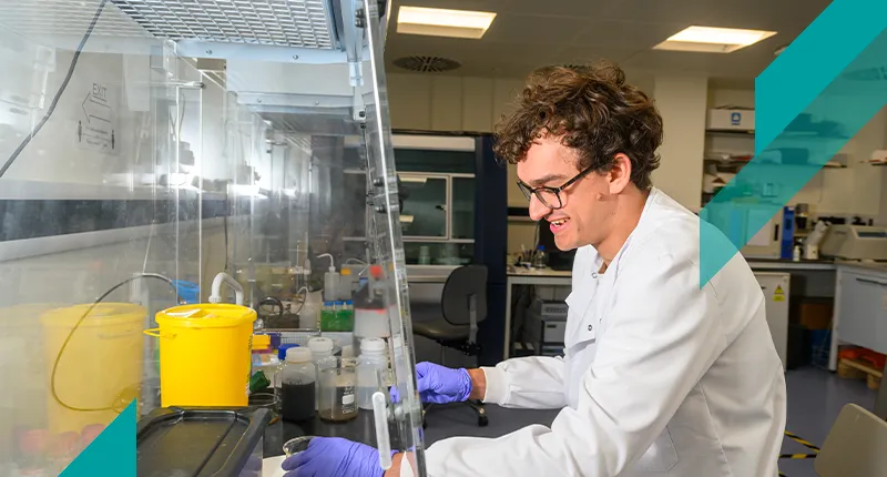 A PhD student works on an experiment in a fume hood in a lab