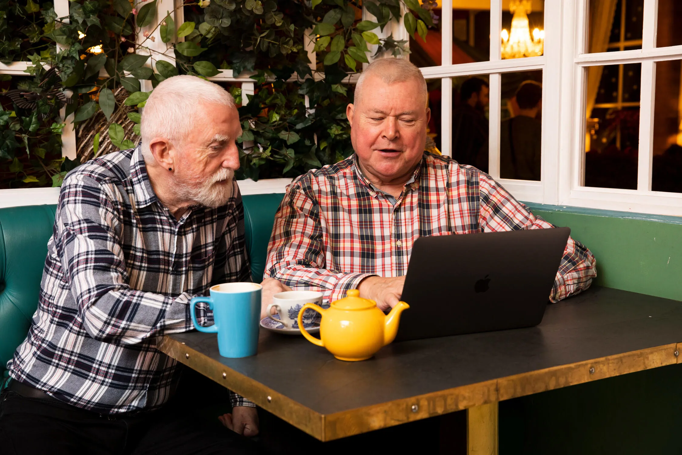 Two elderly men sit looking at a laptop