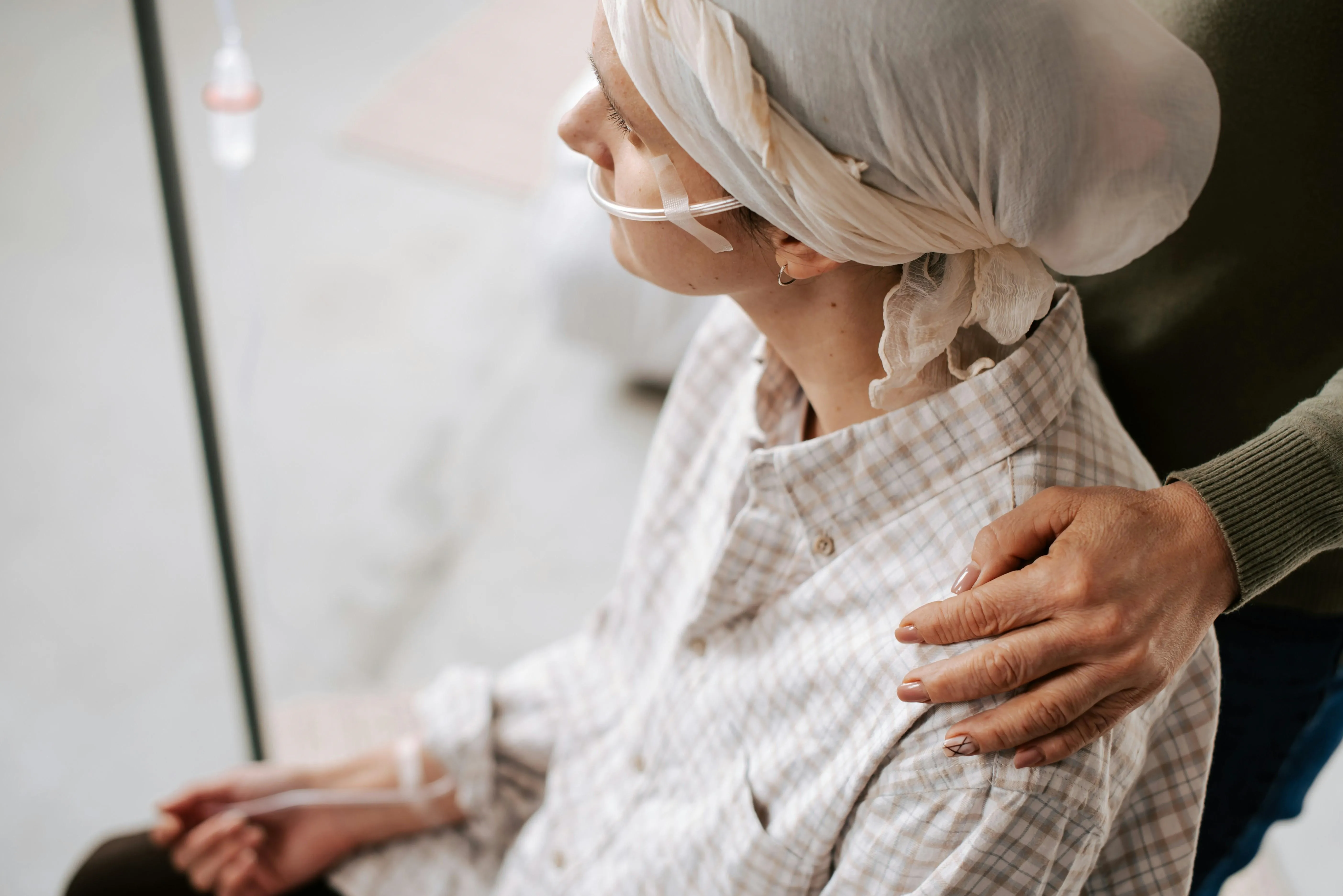 A person with an oxygen tube around their face, an IV drip and sitting in a wheelchair.