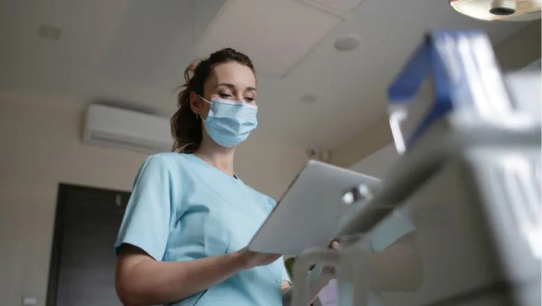 Nurse in a face mask with a clipboard standing by some equipment