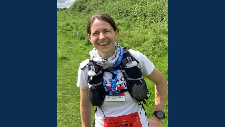 A smiling woman with brown hair tied back in a field. She's in running gear with two water bottles strapped to her chest and a race number pinned to her stomach.