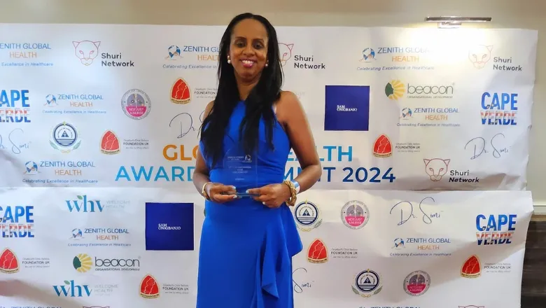 A woman in a blue evening dress stands in front of an awards banner