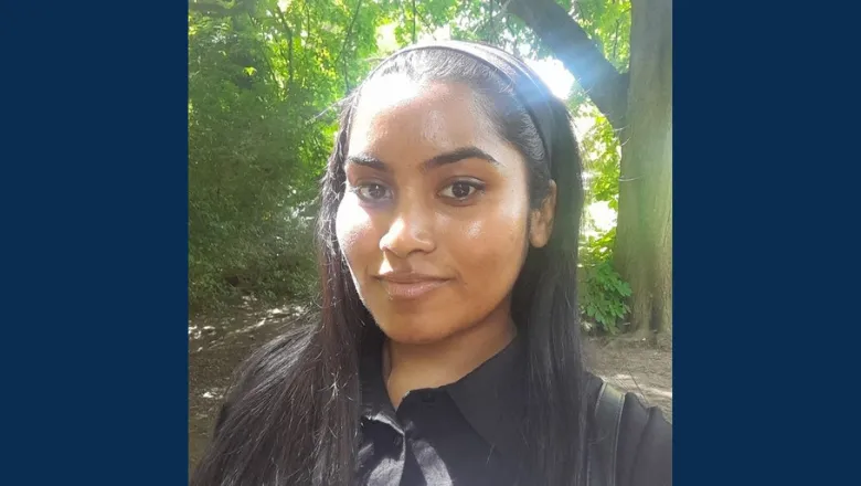 A woman with long black hair takes a selfie outside. A carpet of green leaves can be seen behind her.