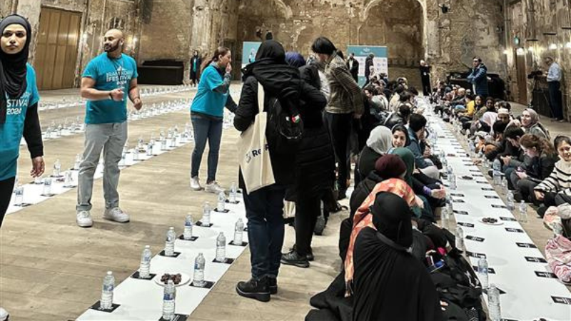 A community iftaar meal held by the Ramadan Tent project in an open space. Muslims are sitting down together getting ready to break their fast.