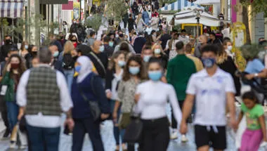 Crowd goes up and down a busy shopping street wearing a protective mask - iStock