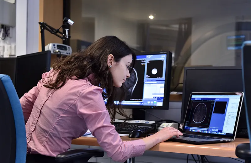 A woman working on a laptop, looking at images of brain scans