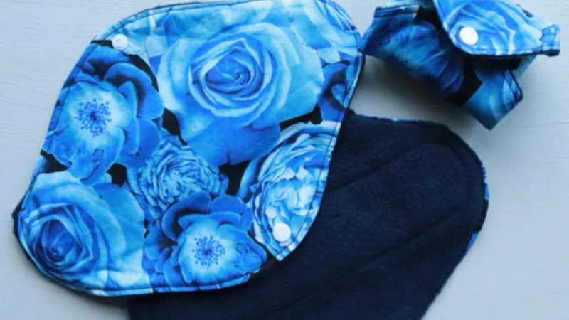 Blue reusable menstrual pad set with a floral pattern, featuring snaps for fastening and a folded compact version.