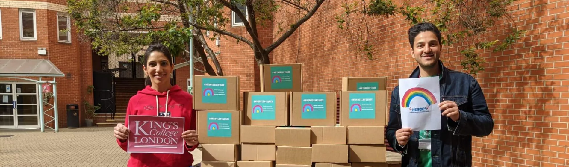 Two people stand either side of a pile of cardboard boxes containing care packages for NHS staff