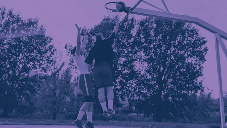 Two women actively playing basketball on a court