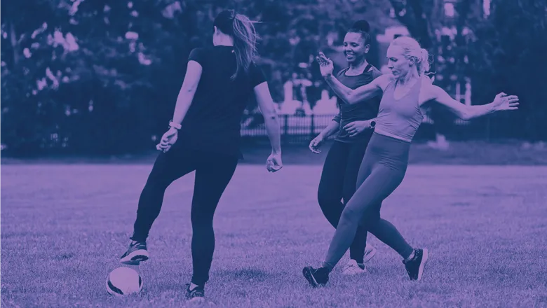 Three women engaged in a football match on a grassy field.