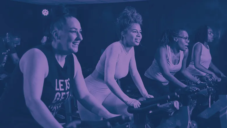  Women participating in a fitness class, riding stationary bicycles in a vibrant gym environment.