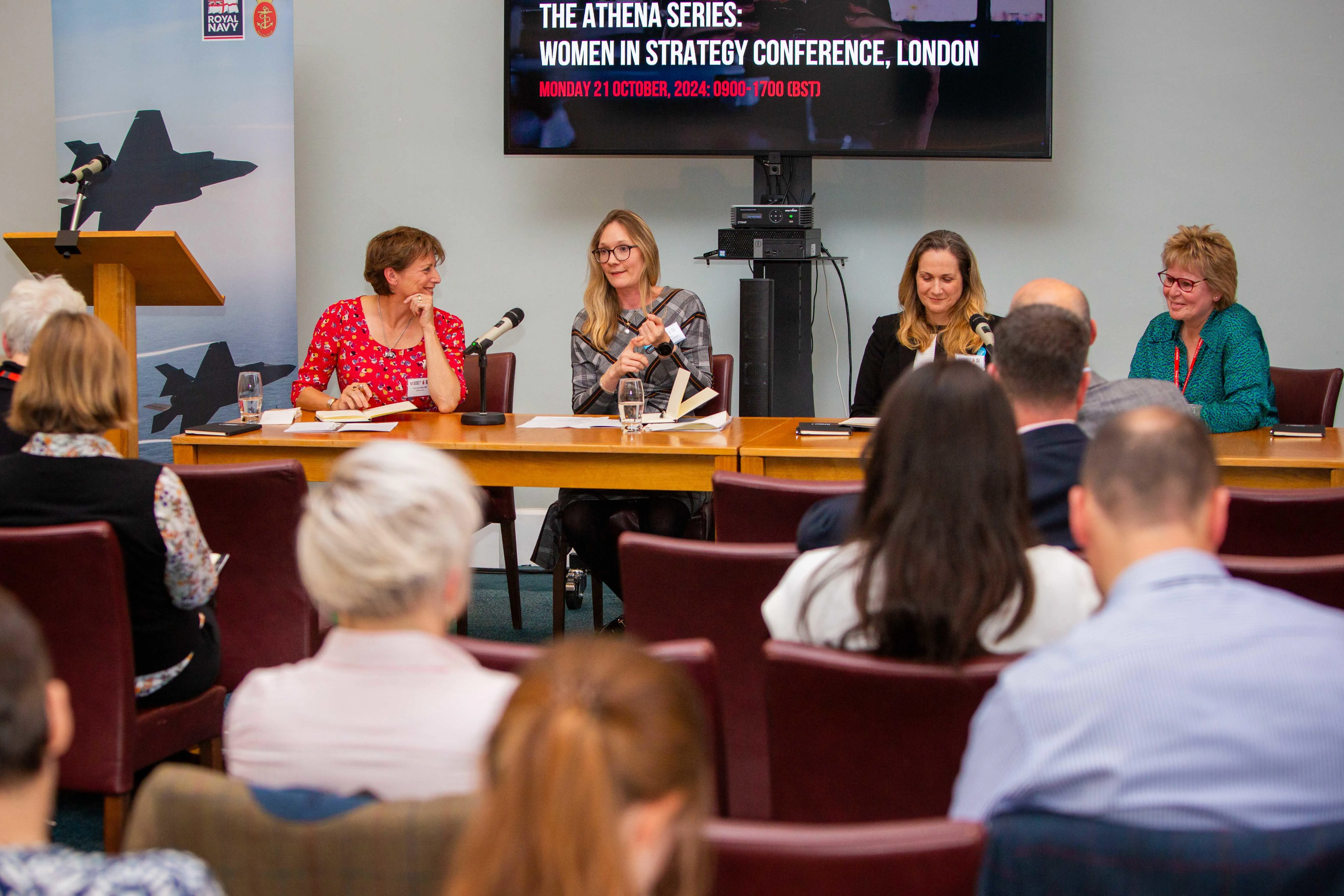 A panel of four people are sat at a table in front of an audience.