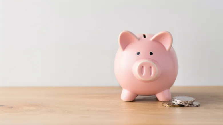 Pink piggybank on wooden table with few coins on the side