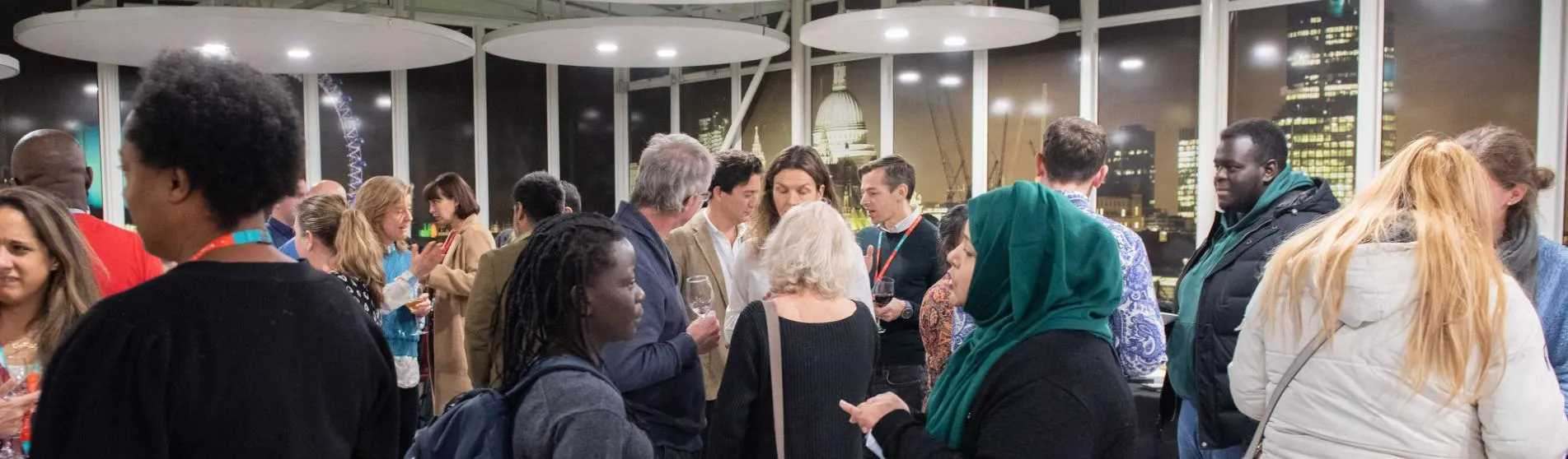 Photo of people talking to each other in groups of 2 or 3 at an evening event.