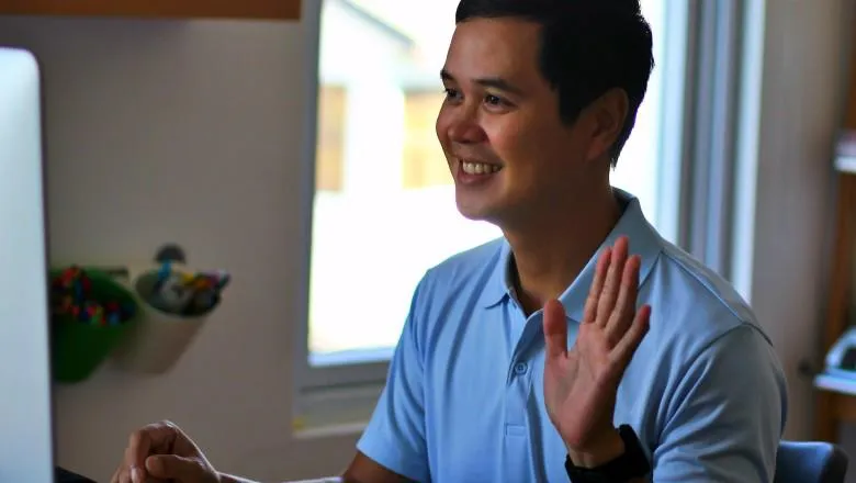 Man waving awkwardly at a computer screen.