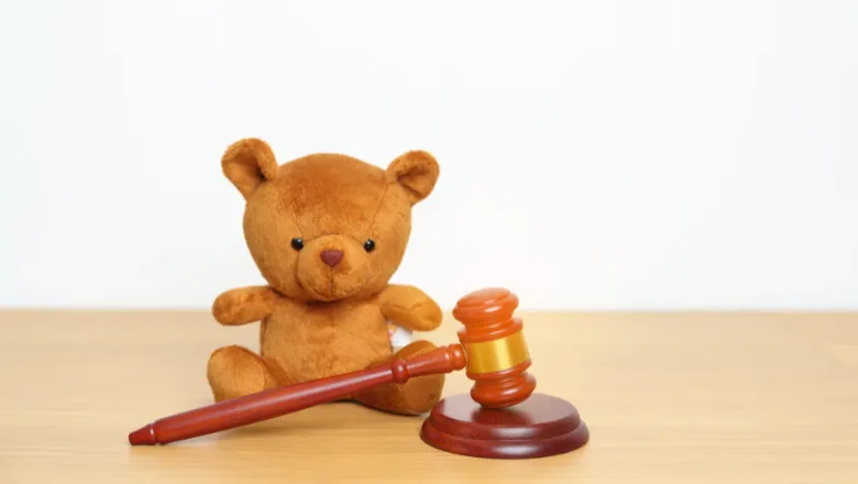 An image of a child's teddy bear next to a hammer and gavel