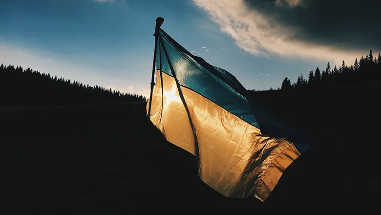 Ukraine flag flying in front of silhouetted landscape and dark skies