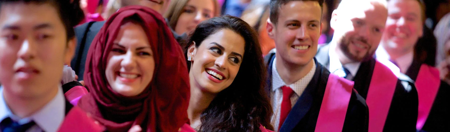 Smiling students wearing black graduation gowns with pink trim