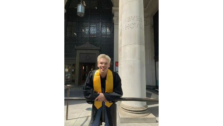 A student wearing graduation gown and yellow stole in front of Bush House