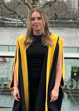 Smiling student in graduation robes by river Thames