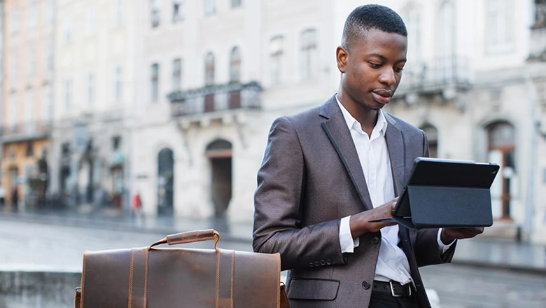 Young finance and banking professional wearing a suit using tablet outdoors. 