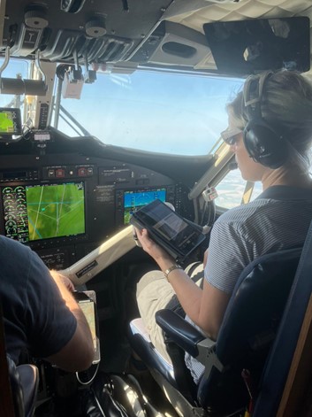 A woman in the cockpit of a small plane watching a screen with headphones on