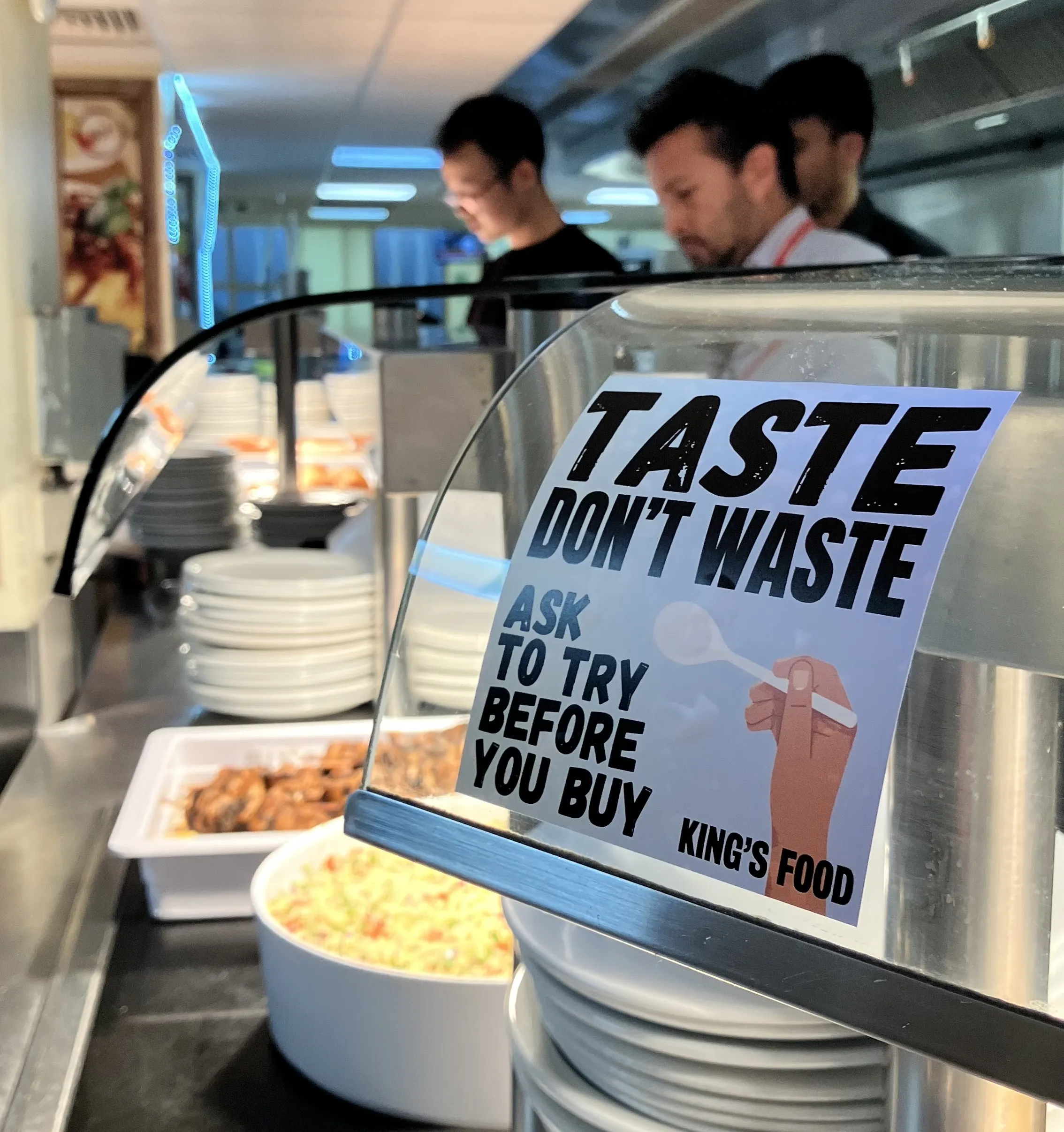 Taste, don't waste sign with bowls of food and a stack of plates in the background.